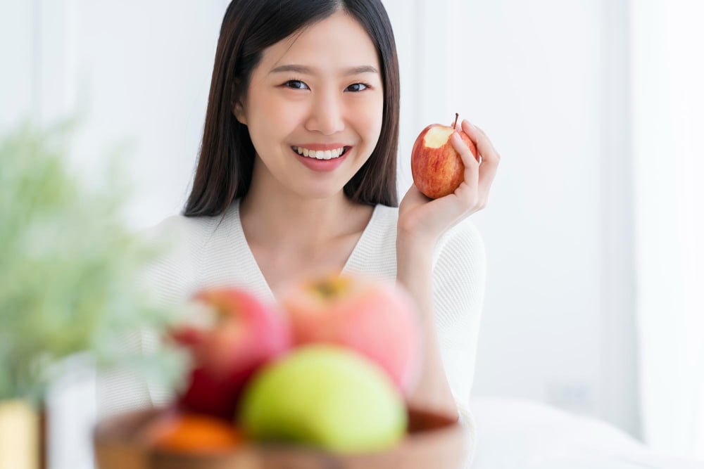 healthy-pretty-asian-woman-happiness-enjoy-eat-love-diet-with-red-fresh-apple-fruit-weight-loss-iedeas-concept-white-room-interior-background A dentist providing instructions on post-extraction care to a patient after a wisdom tooth removal procedure.